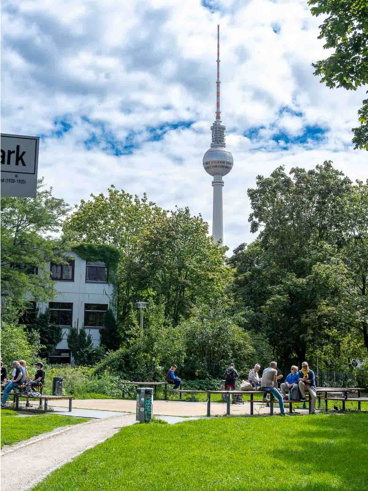 Park with TV Tower: A view of the Berlin TV Tower from a park with people walking and sitting on benches.
