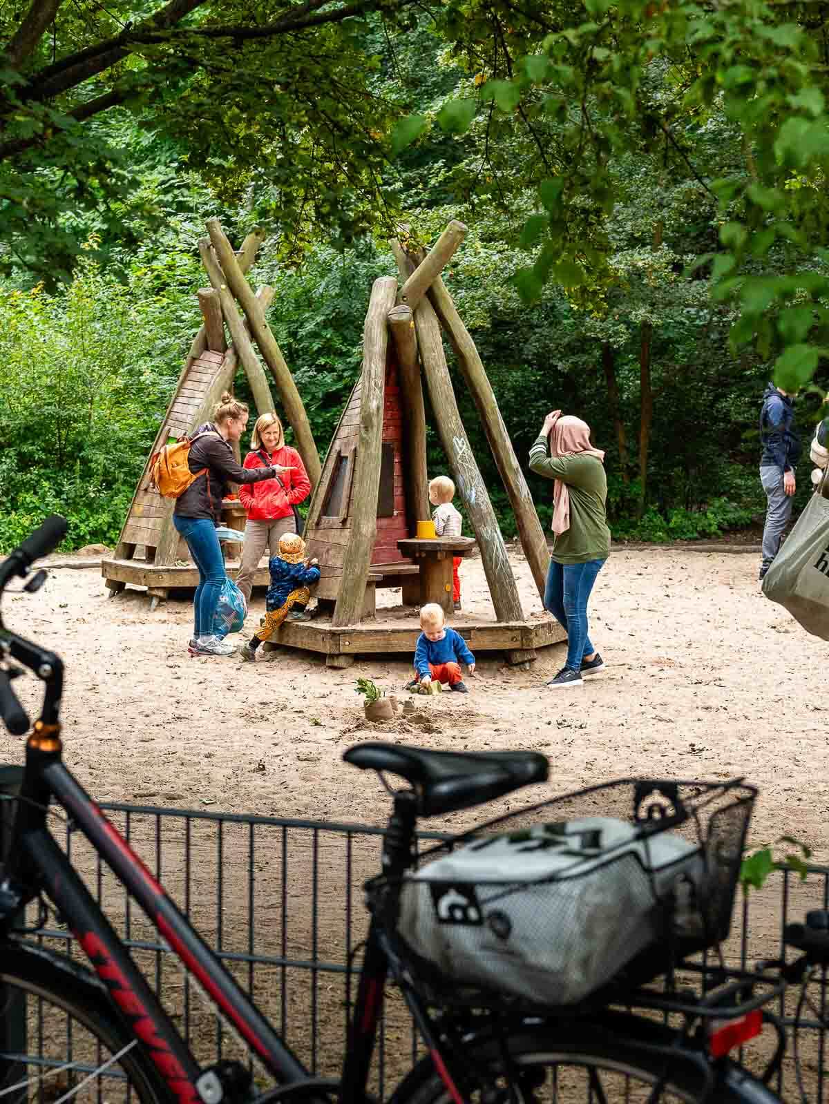 Playground in the Park: Children and parents at a playground with wooden climbing structures.