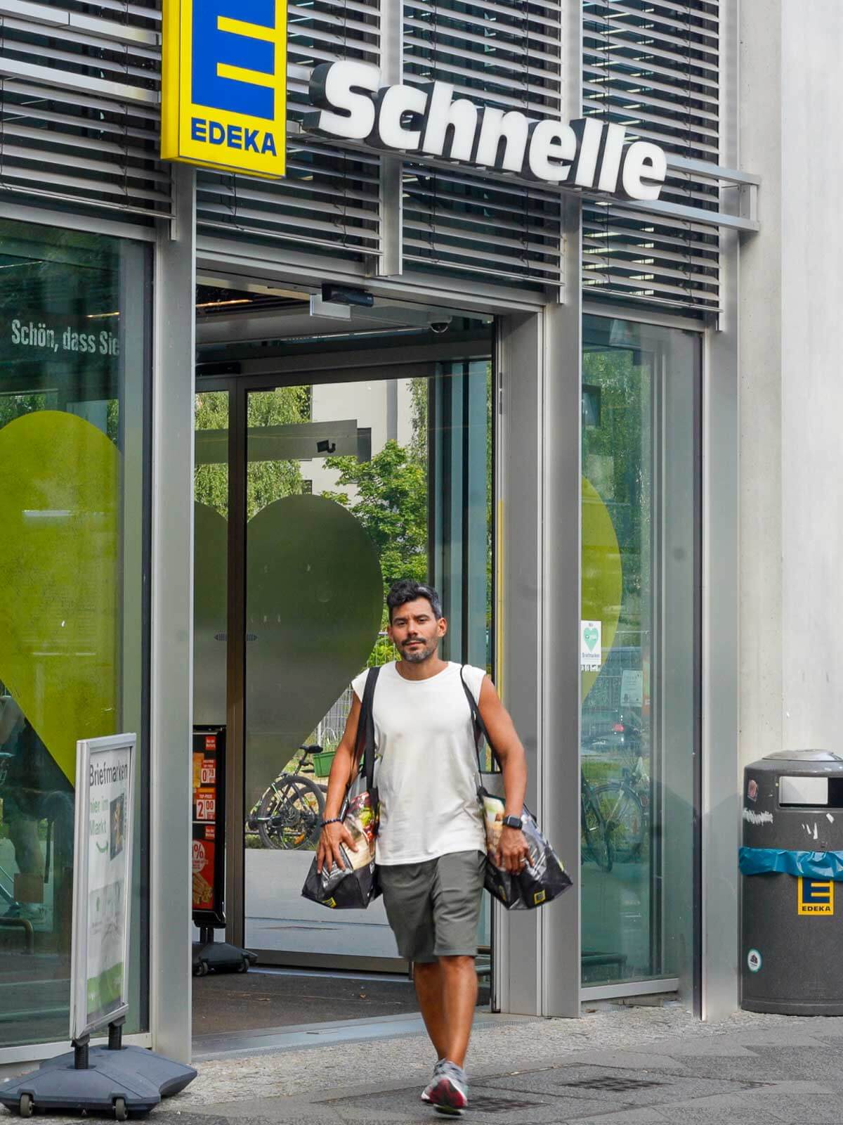 A man walking out of a grocery store carrying a bag of vegan groceries.