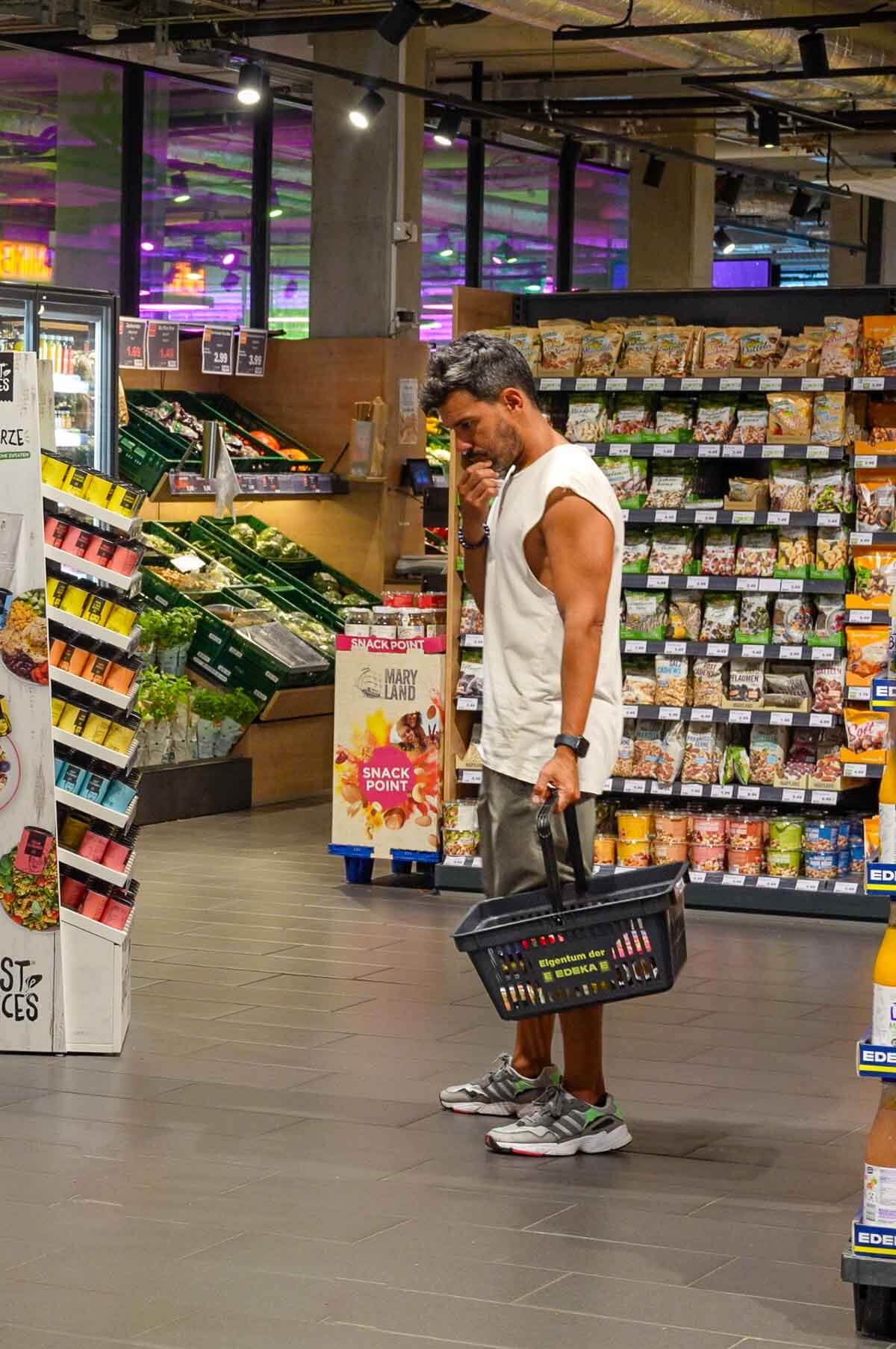 A man browsing the vegan section of a grocery store, holding a shopping basket.