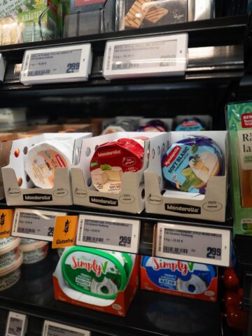 A section of a refrigerated grocery store shelf displaying various vegan dairy alternatives.