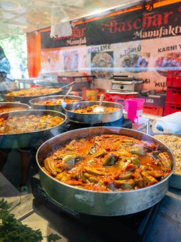 A variety of cooked vegan dishes displayed in large pots at a market or food stall.