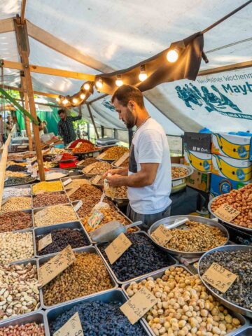 A person shopping at a market stall filled with a variety of grains, nuts, and seeds, in a farmer's market in Neucölln, Berlin.