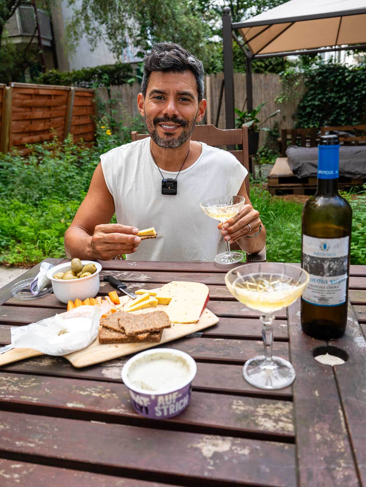 A man sitting at an outdoor table, enjoying a vegan meal with wine and plant-based cheese.