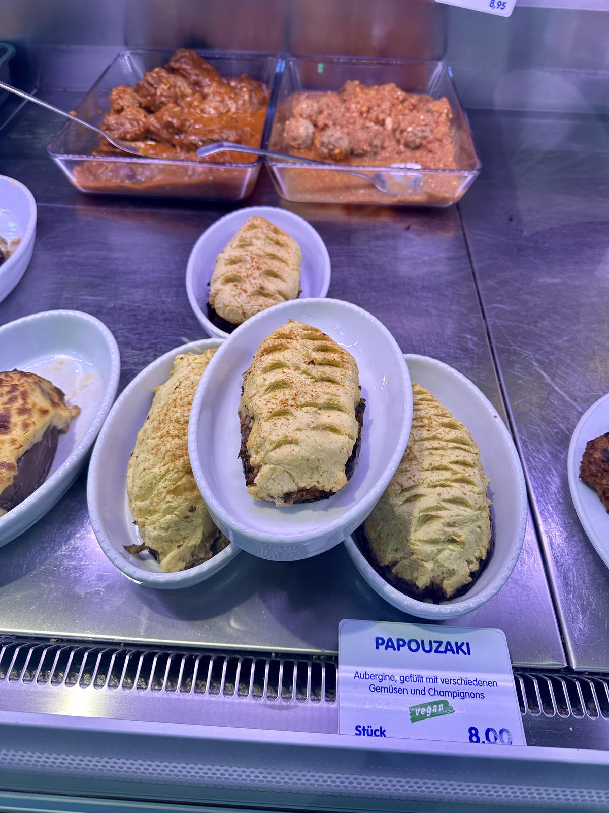 A display of freshly baked Papouzaki, a savory vegan pastry with intricate patterns on top, presented in small white dishes at a food market stall in Kreuzberg.