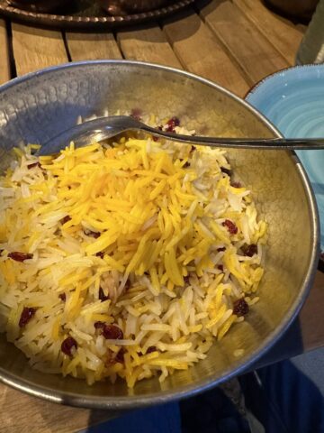 A bowl of fragrant Persian saffron rice mixed with barberries, topped with a generous sprinkle of grated yellow vegan cheese.