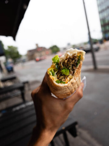 A close-up of a hand holding a vegan falafel filled with greens and vegetables against an urban background in Berlin.