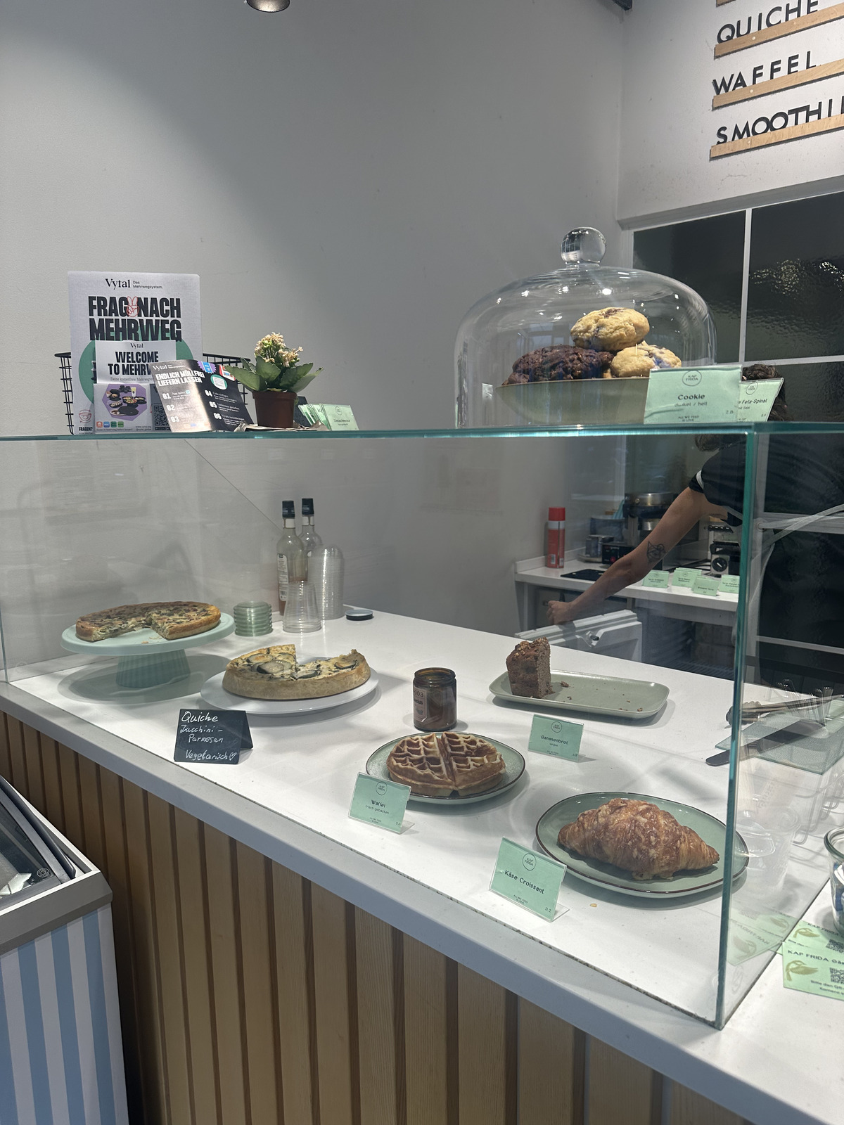 A display case in a vegan bakery featuring a variety of pastries, including muffins, croissants, and other baked goods, all carefully arranged on glass shelves with labels.