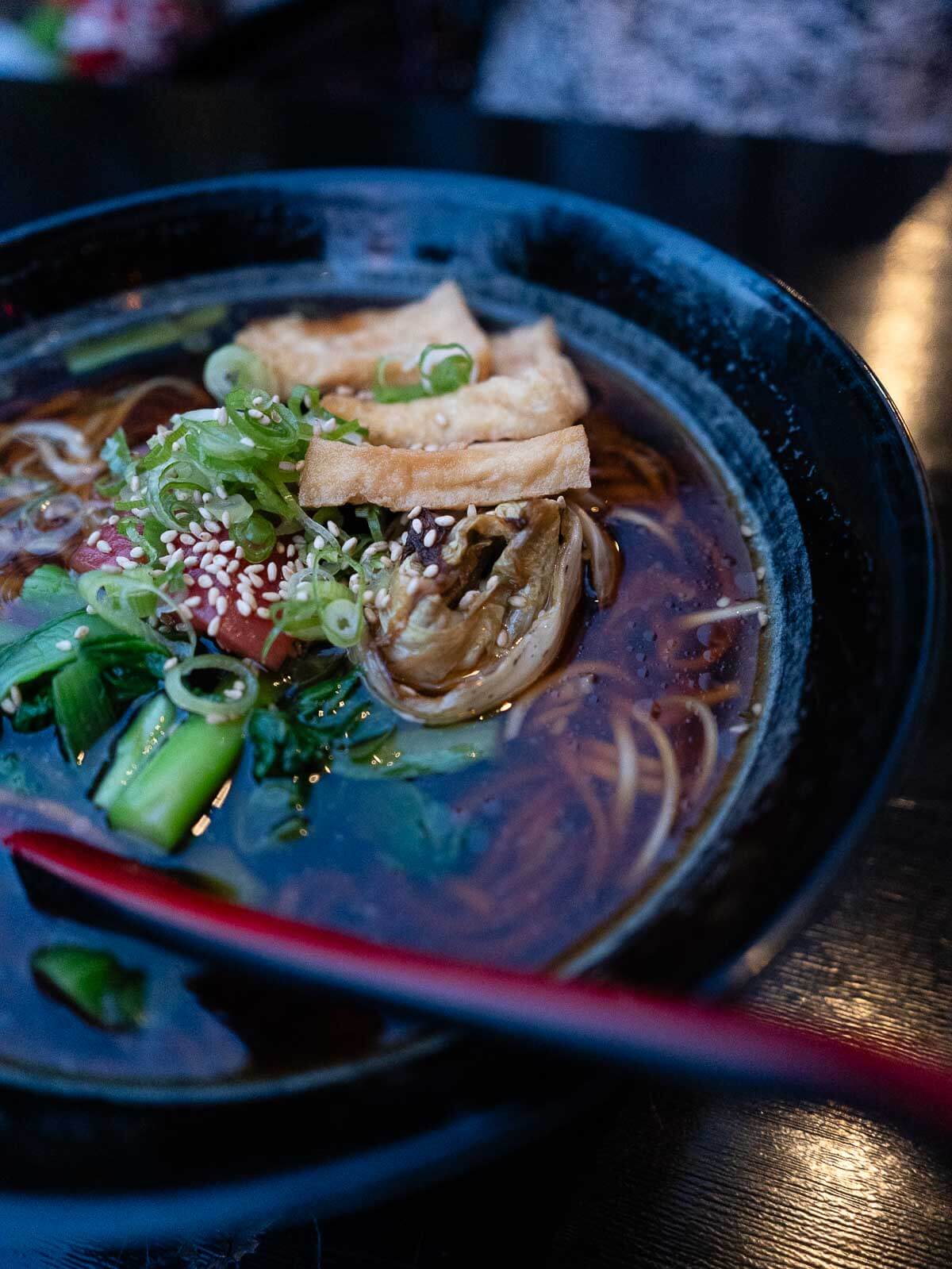 A vibrant bowl of vegan ramen noodle soup garnished with fresh greens and sesame seeds, served at a Berlin café.