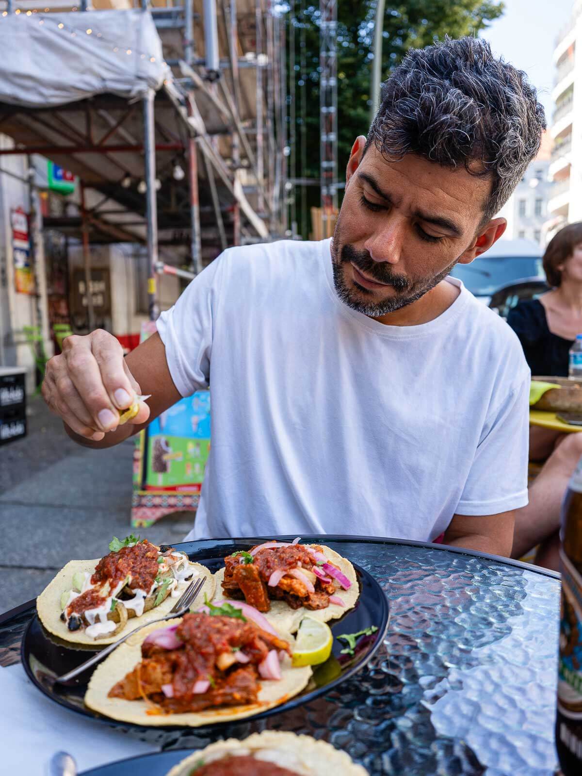 A person enjoying a hearty vegan taco meal with a drink at an outdoor restaurant in Berlin.