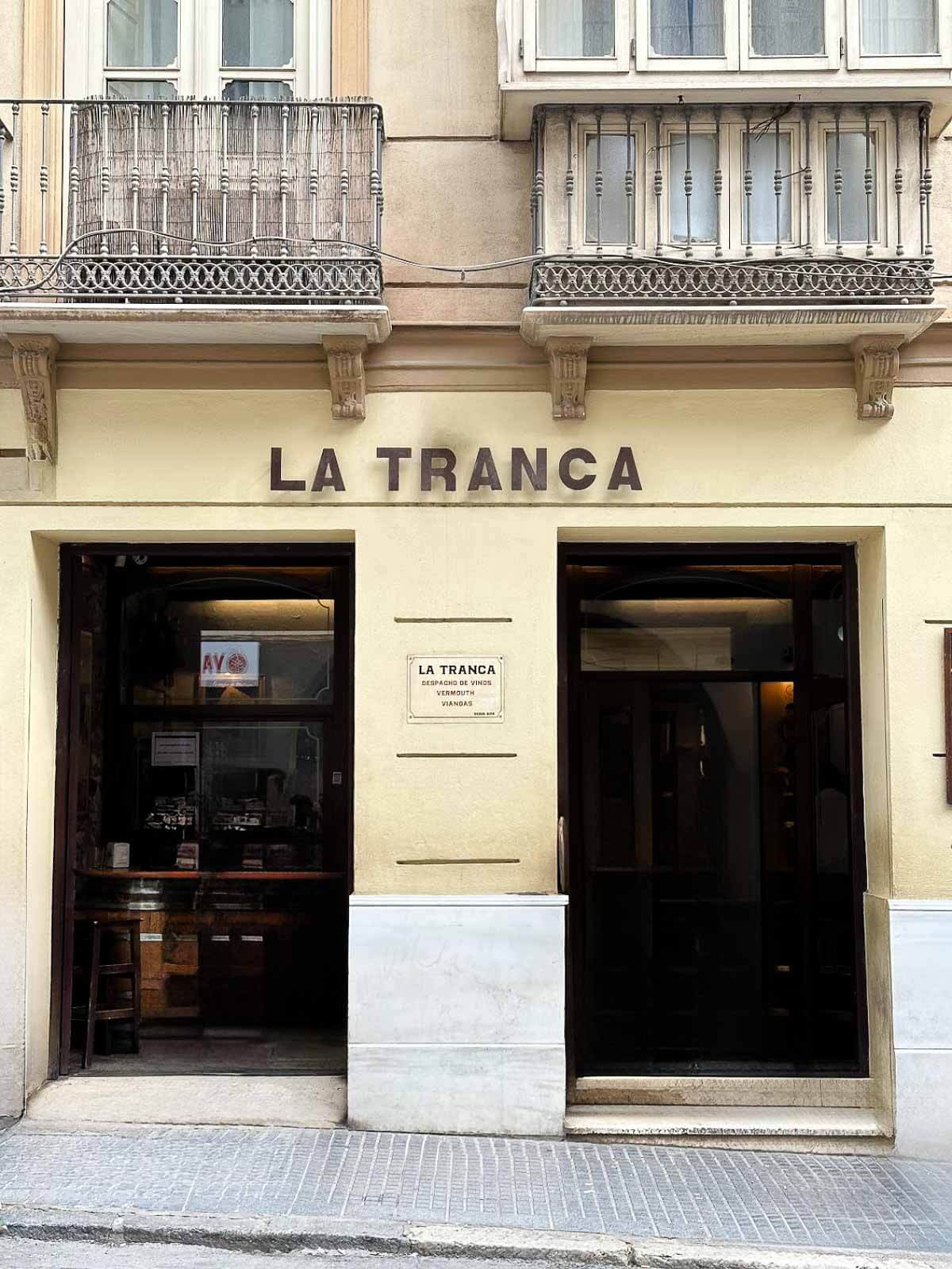 The exterior of La Tranca, a popular tapas bar in Málaga, with a sign above the entrance, inviting locals and tourists to enjoy the lively atmosphere inside.