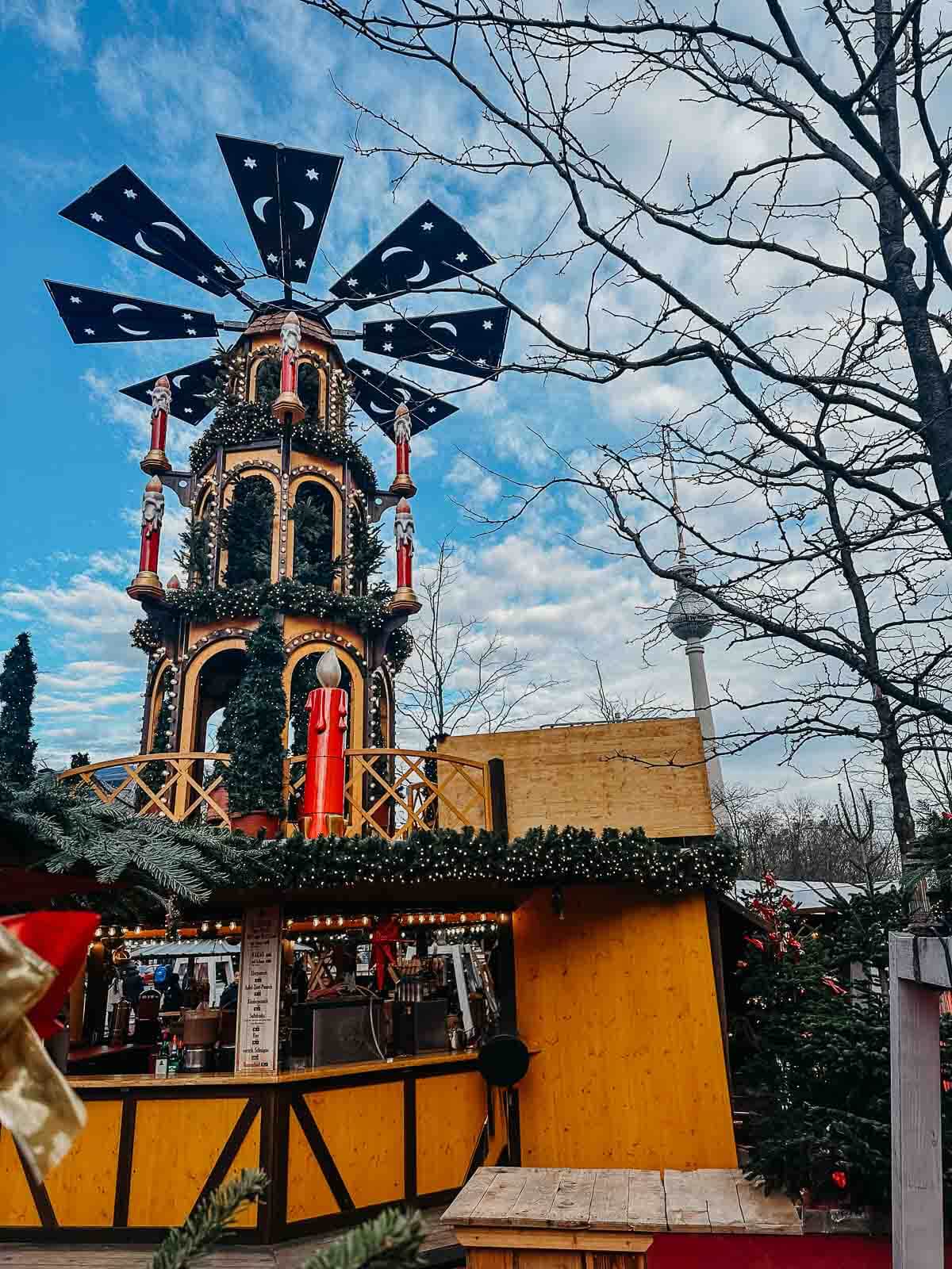 A beautifully lit, multi-level carousel at a Christmas market in Berlin, set against the blue sky.