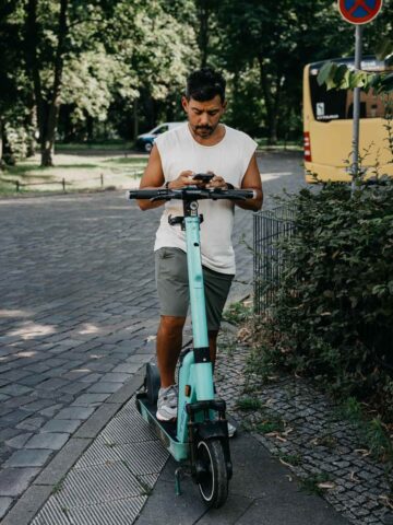 A person riding an electric scooter on a sunny street in Berlin, surrounded by trees and urban scenery.