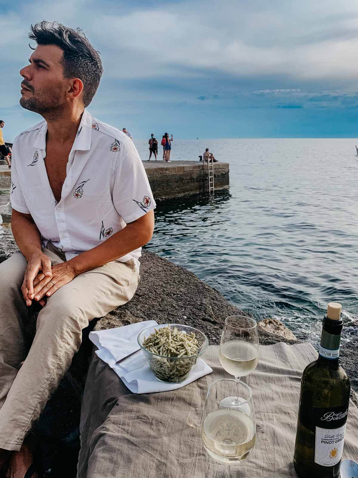 A man having a glass of wine and traditional pasta with pesto genovese.